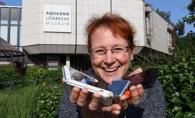 Die stellvertretende Direktorin des Aquazoo, Sandra Honigs, steht vor dem Institut und hält defekte Smartphones und leere Druckerpatronen in den Händen