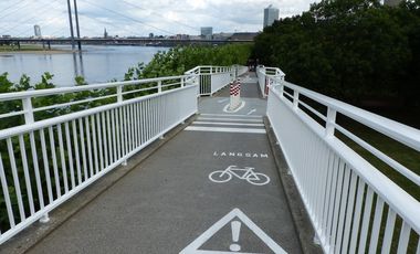 Um die Hafeneinfahrtsbrücke, besonders für Radfahrer, sicherer zu machen, wurden die Geländer des Brückenbauwerkes optimiert und die Bodensohle angepasst. Markierungen auf der Fahrbahn signalisieren jetzt "Achtung Radverkehr Langsam" © Landeshauptstadt Düsseldorf, Amt für Verkehrsmanagement 