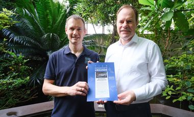 OB Dr. Stephan Keller (r.) erhielt von Aquazoodirektor Dr. Jochen Reiter die Patenschaftsurkunde für das Süßwasserkrokodil "Old Lady". Reiter trägt ein blaues Polohemd und blick tin die Kamera. Er überreicht Herrn Dr. Keller links neben sich die blaue Patenschaftsurkunde, auf der ein Foto des Patentiers abgebildet ist. Auch Herr Dr. Keller im weißen Hemd schaut in die Kamera.