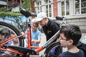 Foto von Kindern, die mit einem Mitarbeiter der Radstation ein Fahrrad reparieren.
