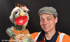 Foto von einem Puppenspieler mit einer Handpuppe. Beide Tragen die Kleidung von Müllmännern.