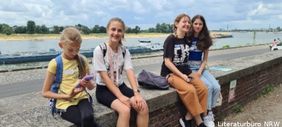Foto mit vier Mädchen, die auf einer Mauer am Rheinufer in Düsseldorf sitzen